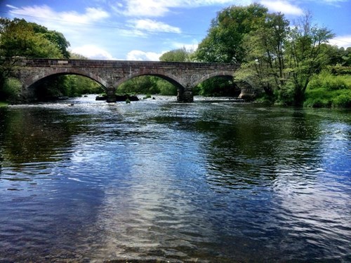 Stone bridge with decorative arches stretching over river, with trees on riverbanks